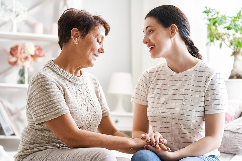 Beautiful mother and daughter are hugging, talking and smiling while sitting on couch at home.