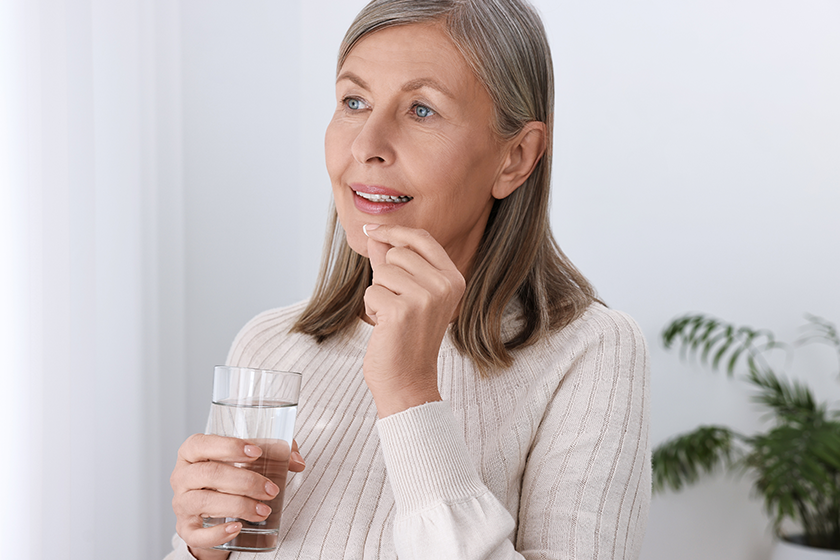 Beautiful woman taking vitamin pill at home 