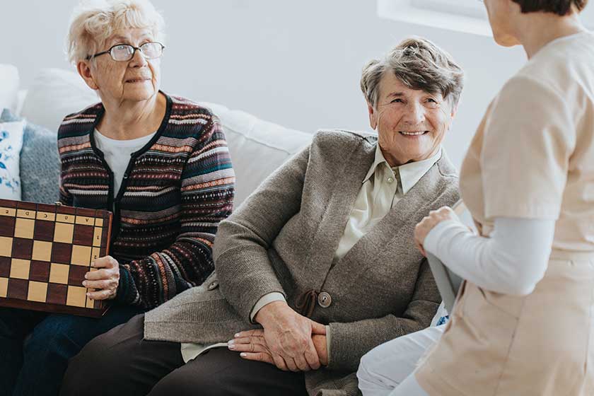 Older ladies sit on a couch and talk to a nurse at a local nursing home