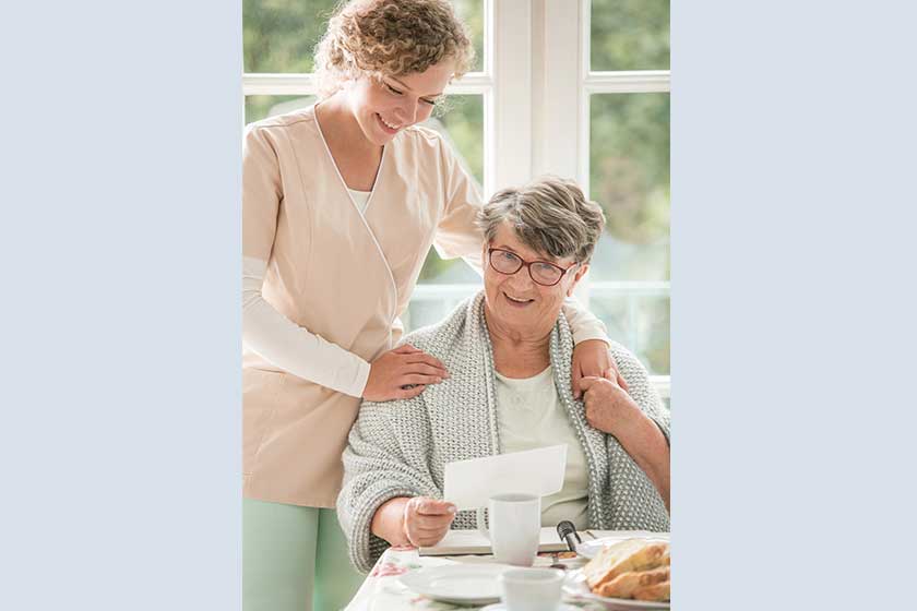 Senior lady on wheelchair with young volunteer in beige uniform supporting her